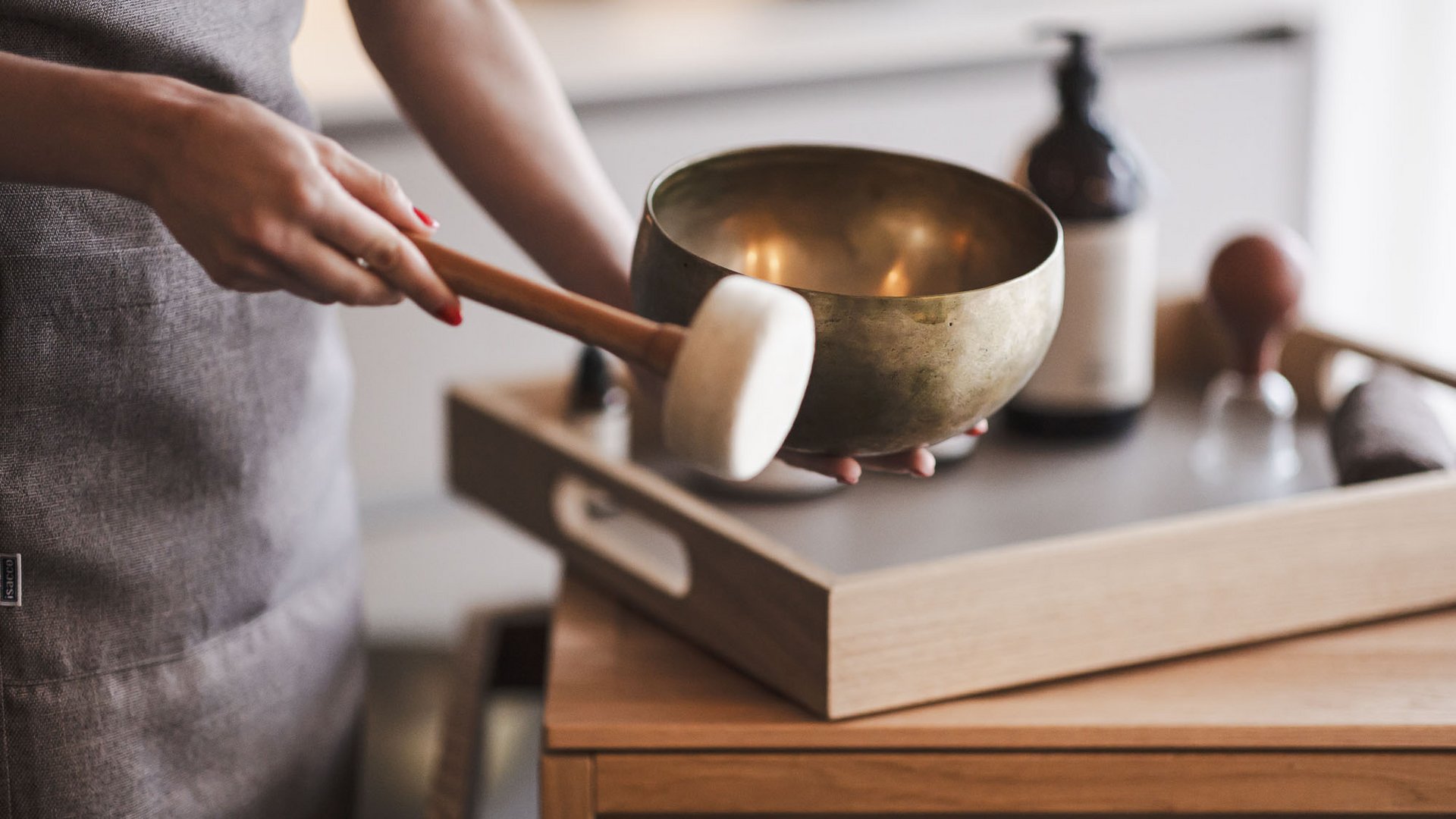 Molto più di una sauna in Val Pusteria: l’Alpenreych Spa Persona che suona una campana tibetana con mazza davanti a un tavolo di legno