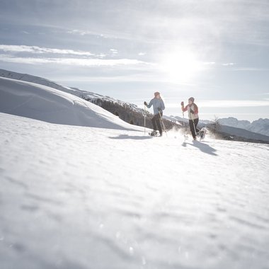 Escursioni invernali in Val Pusteria Due persone a ciaspolare su una collina innevata con il sole brillante