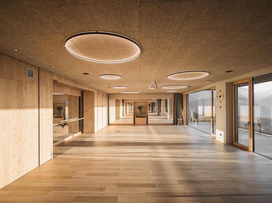 Il nostro hotel a Valdaora tra cielo e terra Ampia stanza con pavimento in legno, parete specchiata e finestre con vista sulle montagne