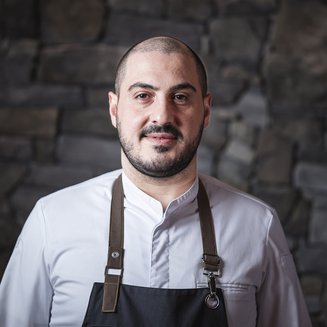 Vivere piaceri culinari stellati Ritratto di un cuoco uomo con giacca bianca e grembiule davanti a muro di pietra