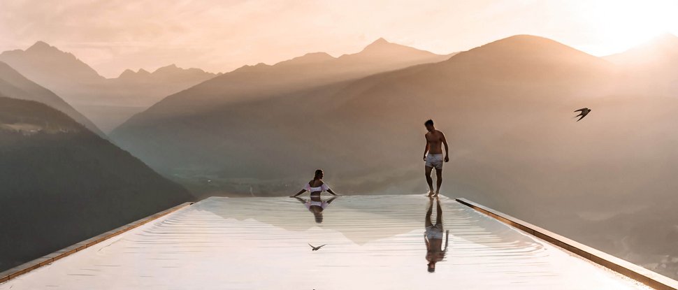 Ultime novità e storie da Valdaora Due persone in una piscina a sfioro con vista sulle montagne al tramonto