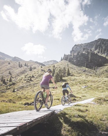 Current news and stories from Olang Two mountain bikers riding on a trail in the mountains on a sunny day