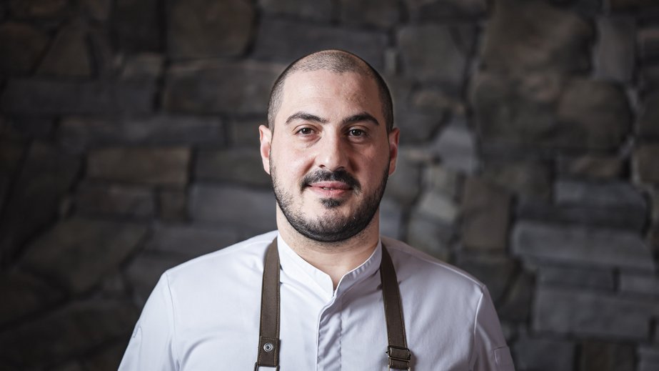 Our 5-star hotel in Italy between heaven and earth Portrait of a chef in white jacket and black apron against a stone wall