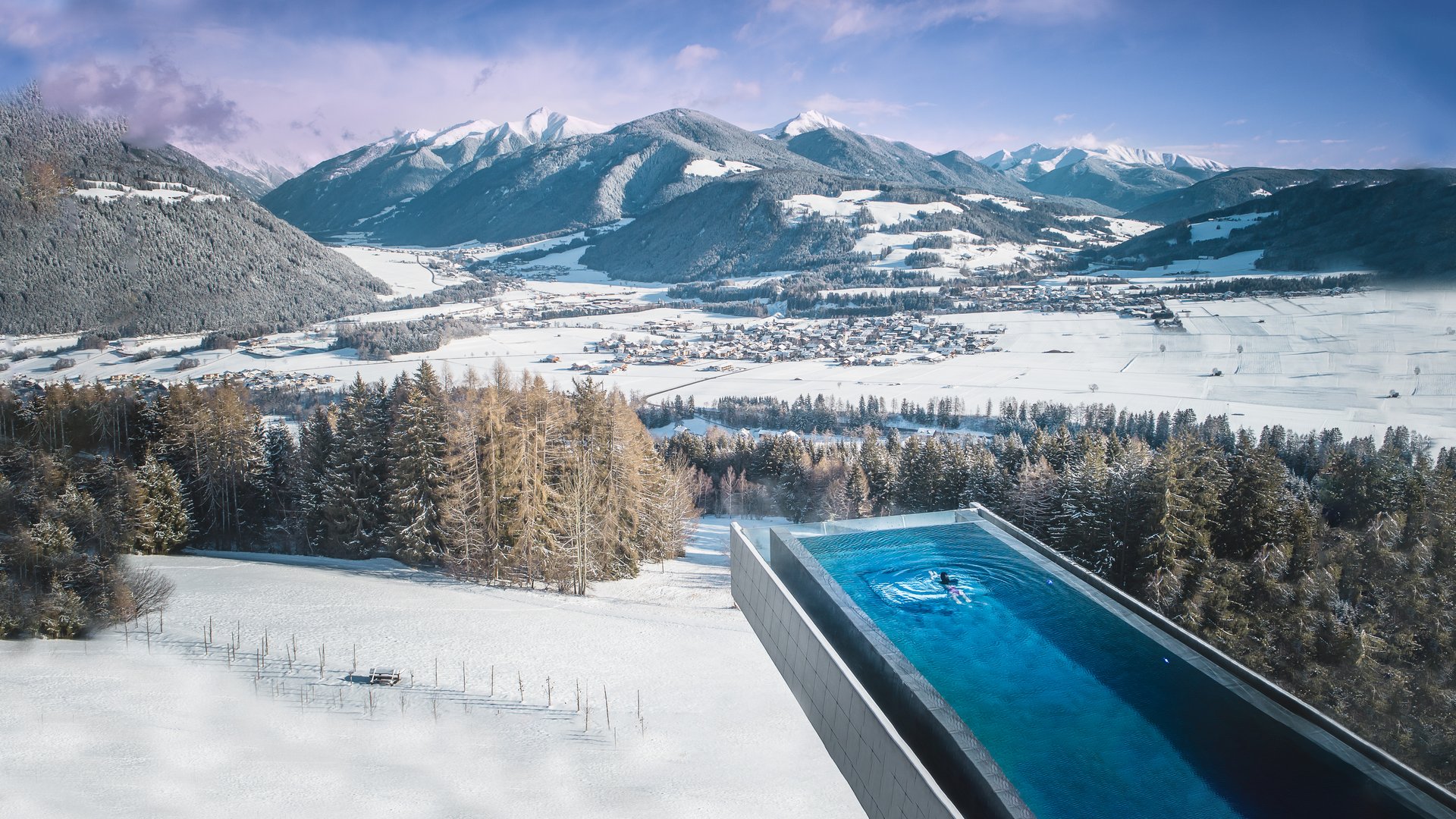 Il nostro hotel a Valdaora tra cielo e terra Piscina a sfioro con vista su montagne innevate e valle in inverno