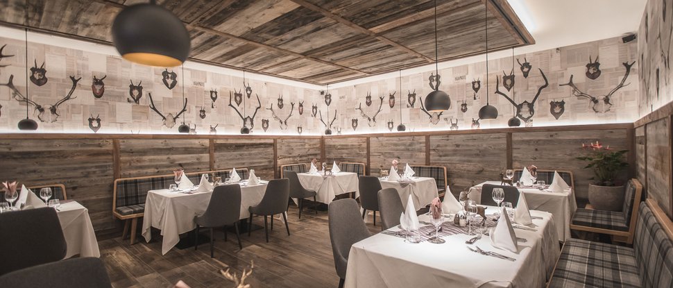Ultime novità e storie da Valdaora Ristorante accogliente con soffitto in legno, pareti con trofei e tavoli apparecchiati