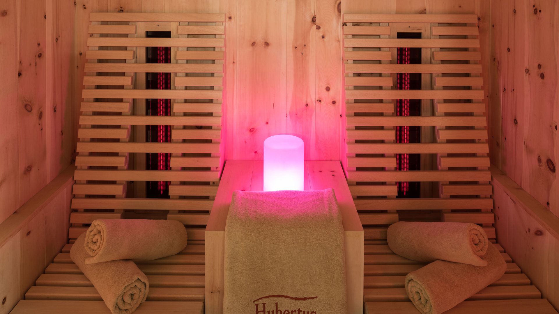 Le nostre saune in Val Pusteria vicino al Plan de Corones Area sauna con sedute in legno, asciugamani e luce rossa soffusa