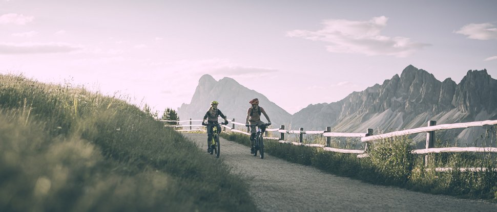 Ultime novità e storie da Valdaora Due ciclisti su un sentiero di montagna con recinzione e montagne sullo sfondo