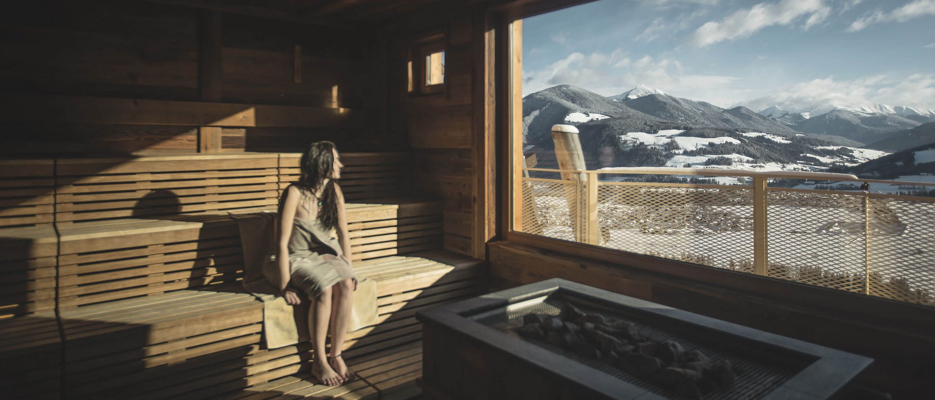 Benessere su tutte le sfaccettature dell’essere Donna in sauna che guarda le montagne innevate da grande finestra panoramica