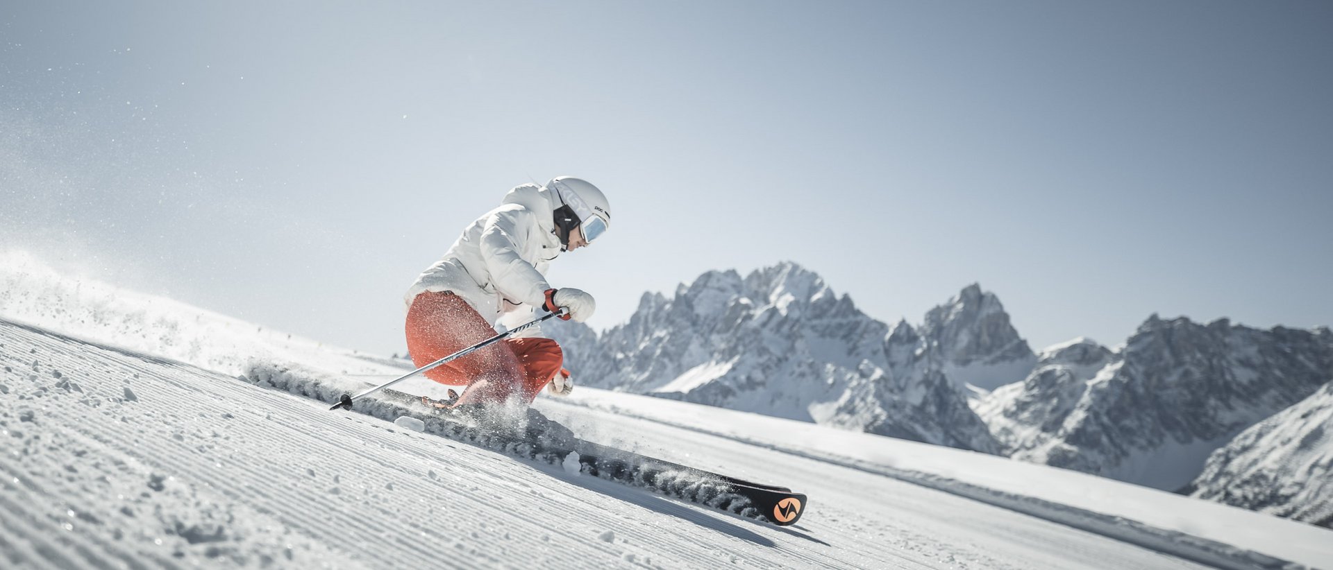 Il vostro hotel al Plan de Corones a 5 stelle Scalatore con giacca bianca e pantaloni arancioni su pista innevata con montagne
