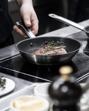 Vivere piaceri culinari stellati Mano che tiene il manico della padella con carne e erbe in padella sulla stufa