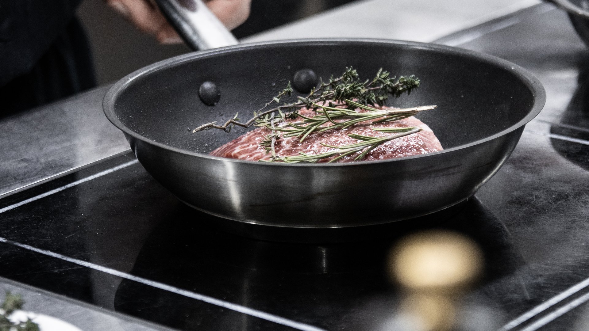 Vivere piaceri culinari stellati Mano che tiene il manico della padella con carne e erbe in padella sulla stufa