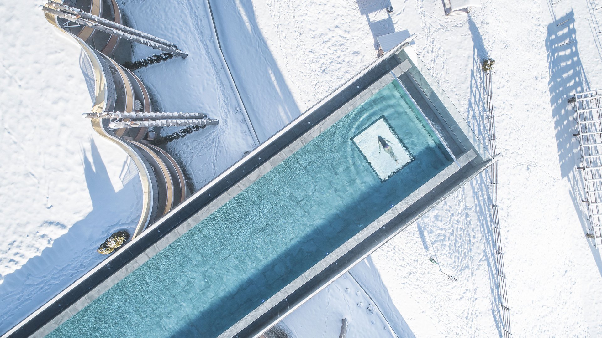 Piscina sopra un paesaggio innevato con persona che nuota vista dall'alto