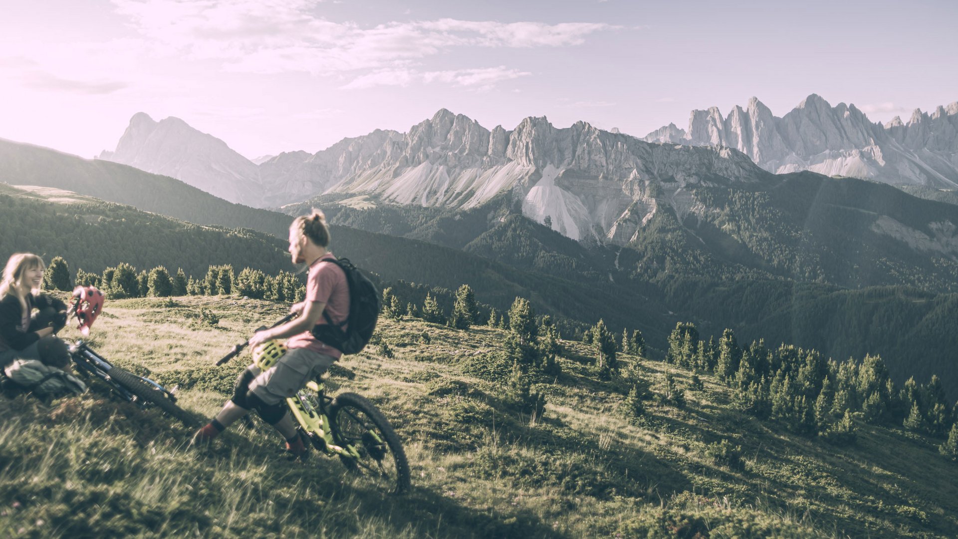 Il nostro programma estivo settimanale Due mountain biker si riposano su un prato con panorama montano alle spalle
