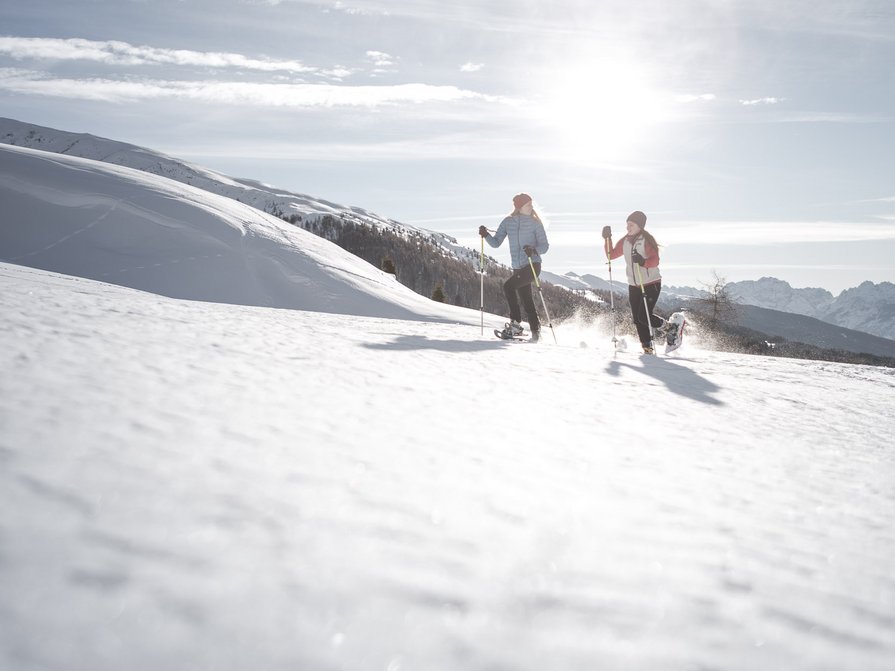 Il nostro hotel a Valdaora tra cielo e terra Due persone camminano con le racchette da neve nella neve soleggiata in montagna