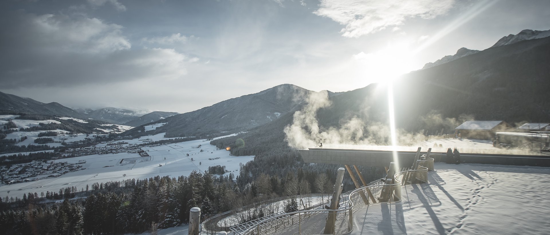 Hotel in Val Pusteria con spa per il vostro relax Vista invernale soleggiata su montagne e valle innevate con fumo sopra il tetto