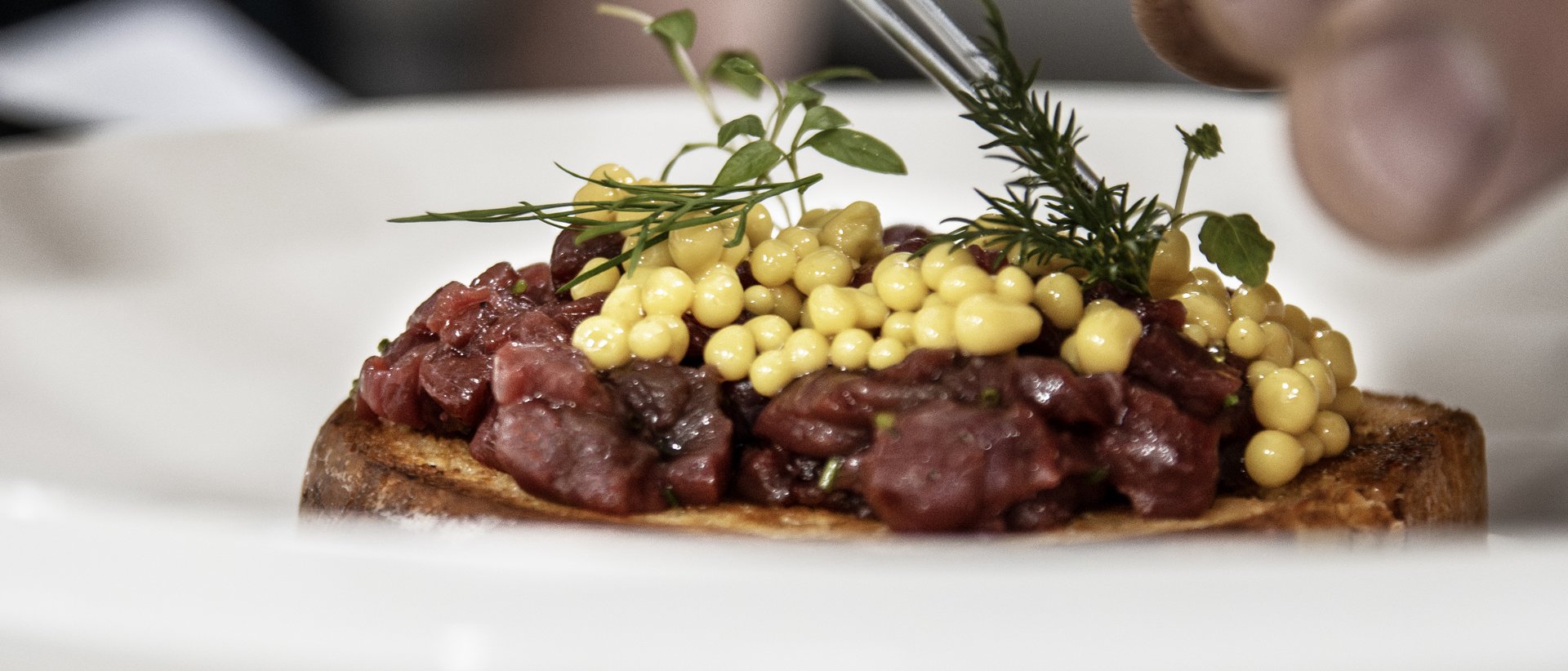 Hotel gourmet in Alto Adige per buongustai Mani che decorano un piatto con erbe fresche e perle gialle