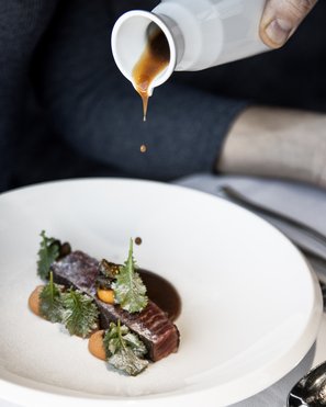 Vivere piaceri culinari stellati Salsa versata su un pezzo di carne finemente guarnito su piatto bianco