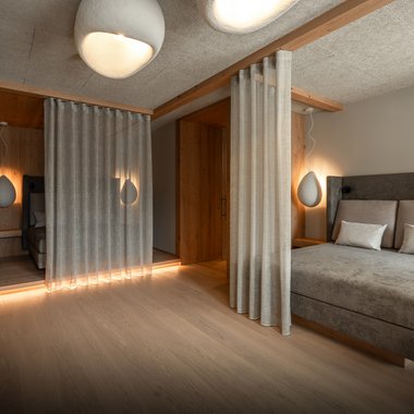 Hotel in Val Pusteria con spa per il vostro relax Camera da letto moderna con letto grigio, tende e luci soffuse