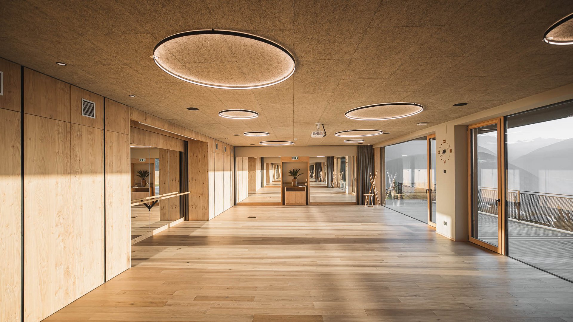 Il nostro hotel con palestra in Val Pusteria Sala danza vuota moderna con pavimento in legno e grandi finestre con vista sulle montagne