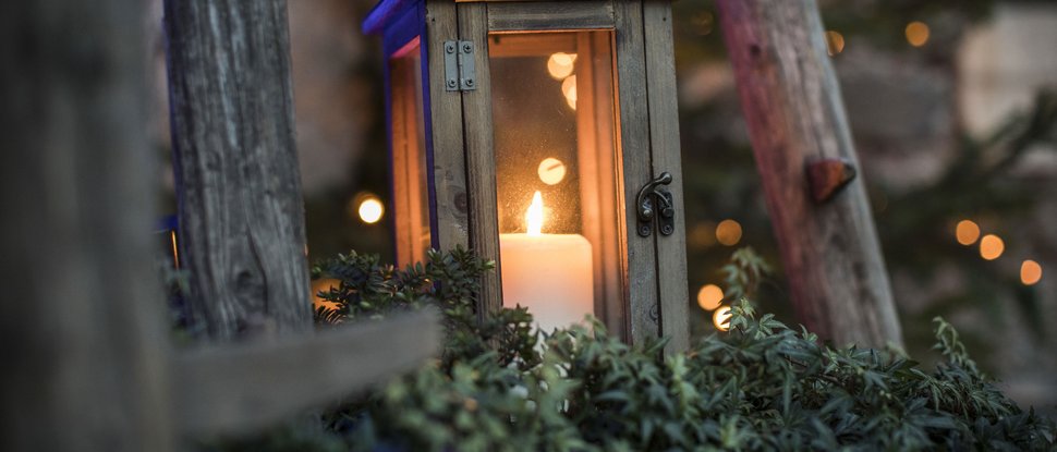 Current news and stories from Olang Lit candle in a wooden lantern surrounded by plants and wooden beams at dusk