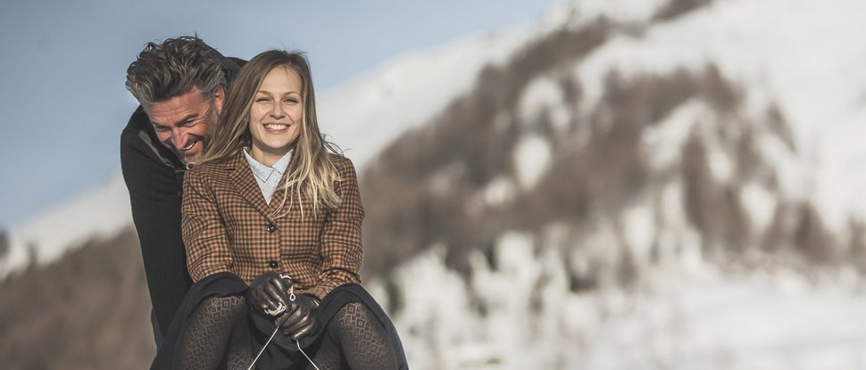 Ultime novità e storie da Valdaora Coppia felice che scivola su una slitta sulla neve con montagne innevate sullo sfondo