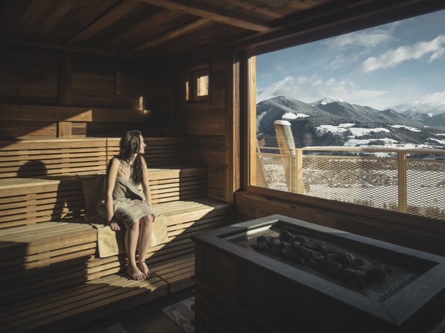 Il nostro hotel a Valdaora tra cielo e terra Donna seduta in sauna con vista sulle montagne innevate