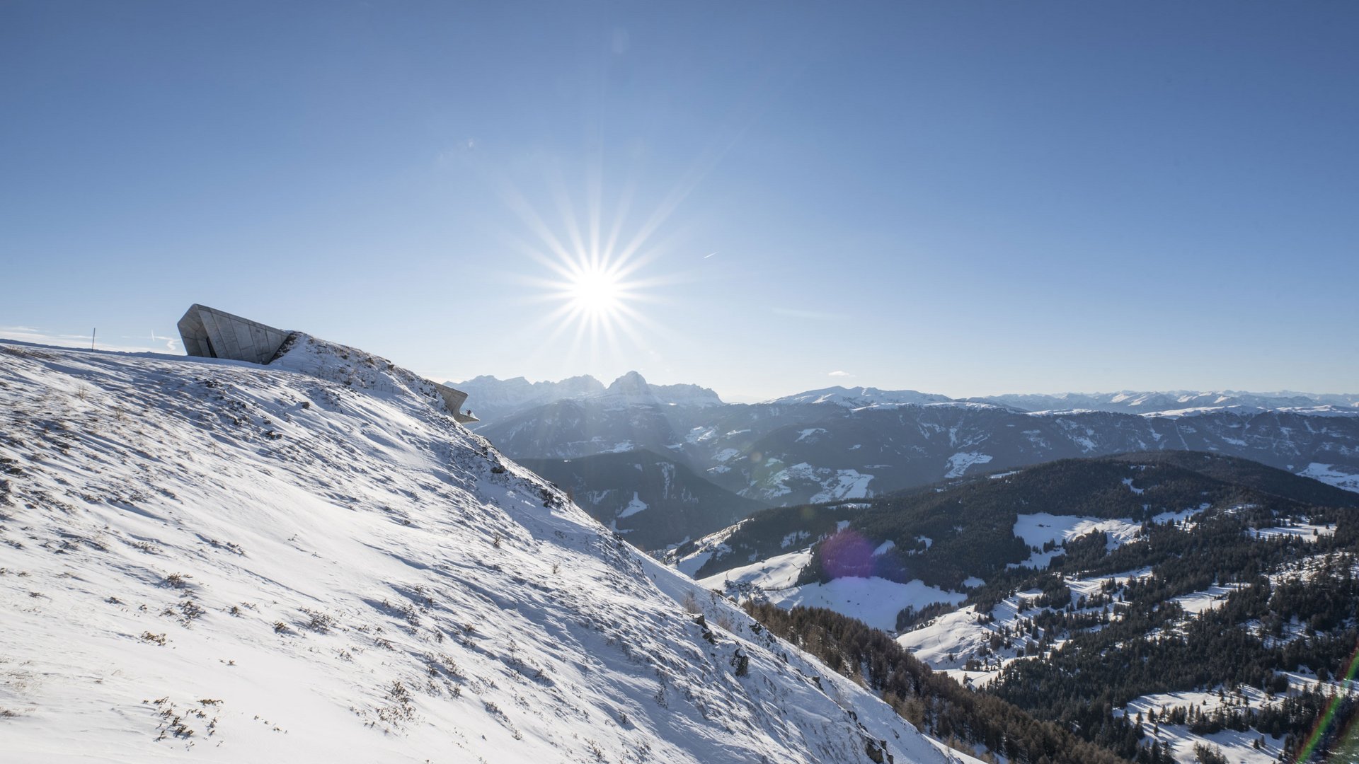 Montagna innevata con sole e montagne lontane sullo sfondo
