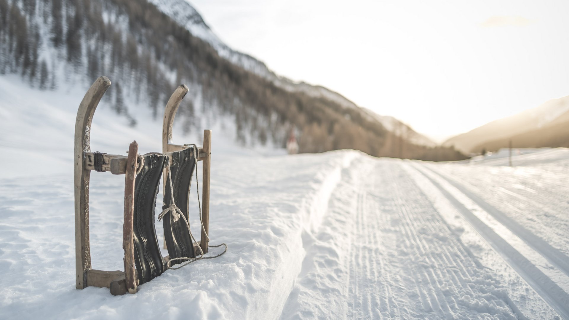 Vacanza a Plan de Corones: un’avventura Vecchia slitta di legno appoggiata sulla neve vicino a una strada innevata di montagna