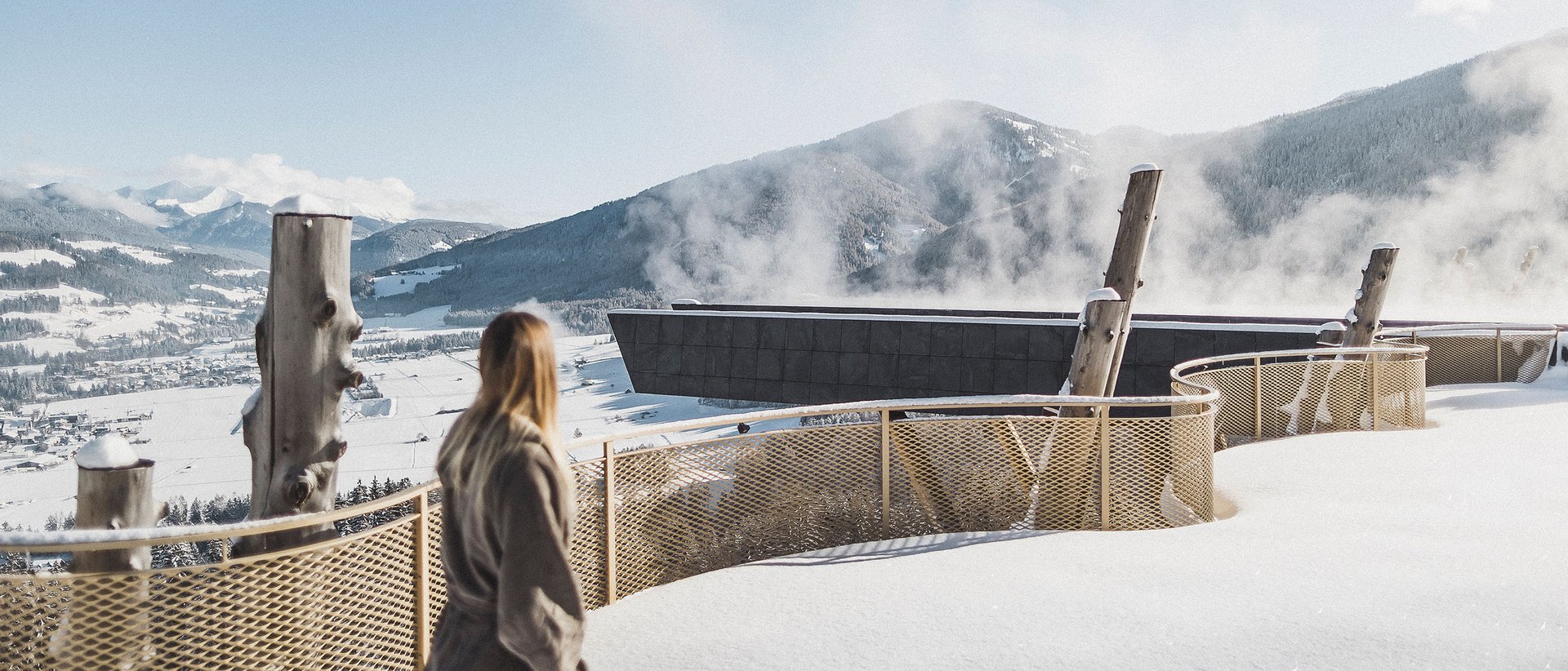 Hotel a 5 stelle in Val Pusteria Donna guarda montagne innevate con edificio fumante e recinzione gialla