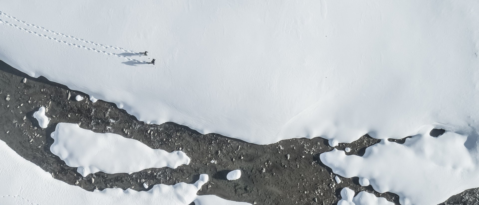 Vacanza a Plan de Corones: un’avventura Vista aerea di due persone che camminano sulla neve vicino a un fiume