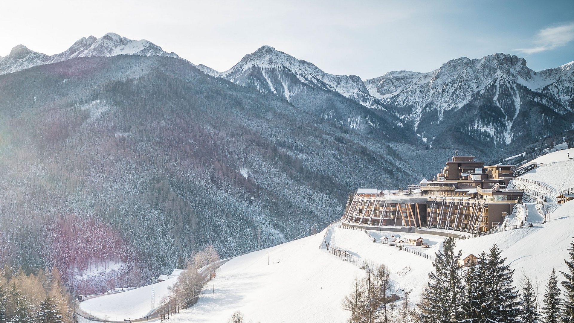 Hotel sulla montagna innevata con alberi di pino e cime rocciose sullo sfondo