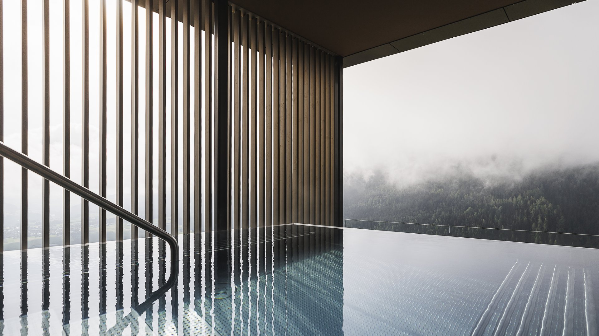 Piscina interna moderna con parete di vetro e vista su foresta nebbiosa