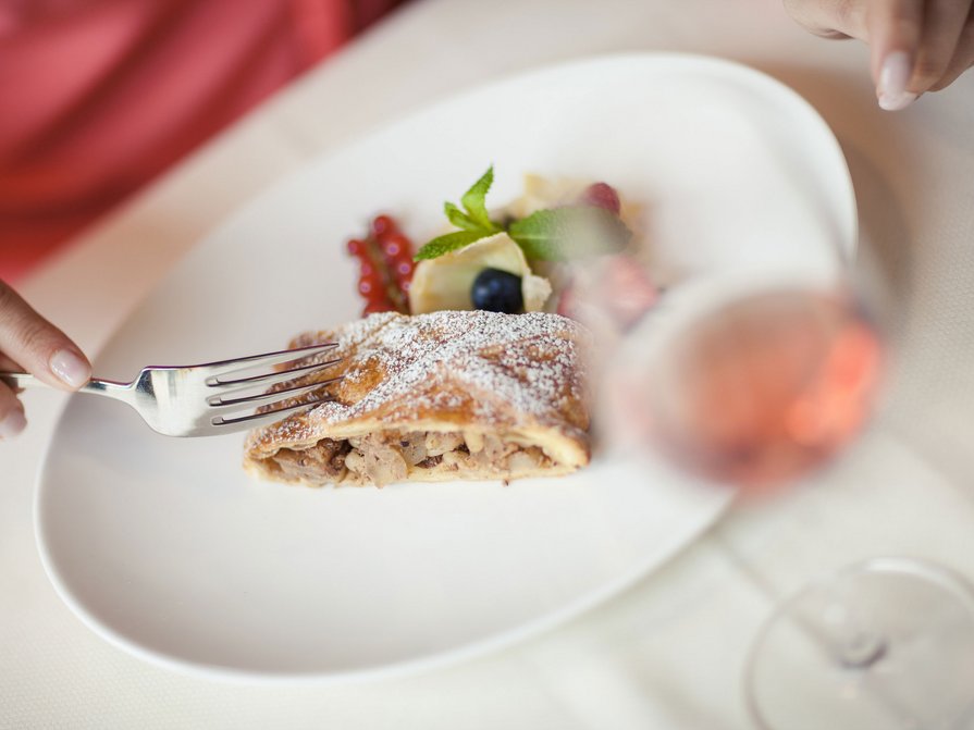 Il nostro hotel a Valdaora tra cielo e terra Persona che taglia strudel di mele con frutti di bosco su piatto bianco