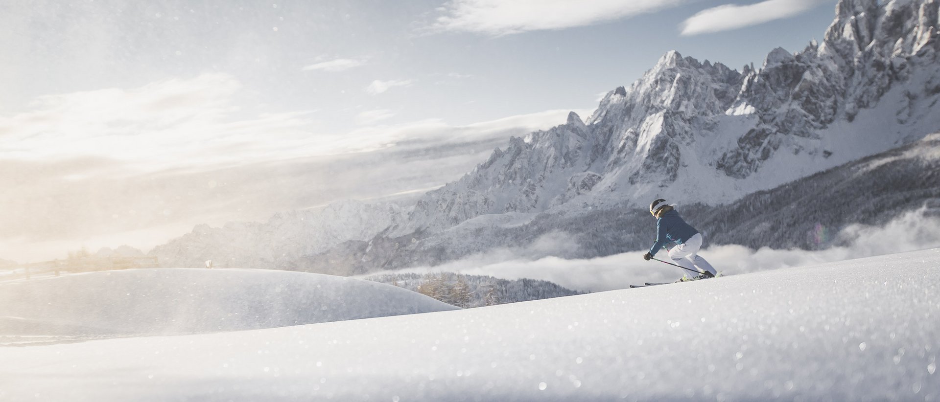 Hotel a 5 stelle in Val Pusteria Sciatore scende sulla neve con montagne innevate sullo sfondo al tramonto