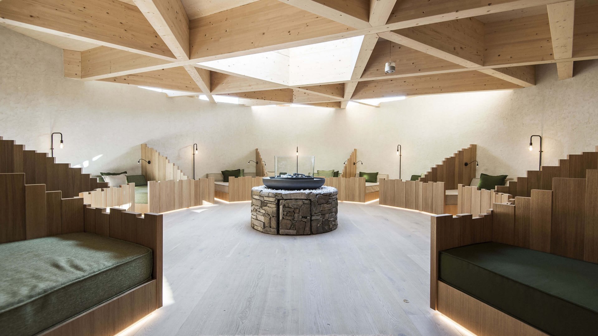 Le nostre saune in Val Pusteria vicino al Plan de Corones Sala relax moderna con soffitto in legno e aree salotto attorno a un camino in pietra centrale