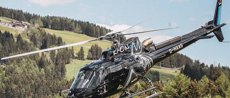 Ultime novità e storie da Valdaora Elicottero nero vola sopra colline boscose con case sullo sfondo