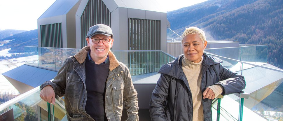 Current news and stories from Olang Two people leaning on glass railing in front of modern mountain architecture