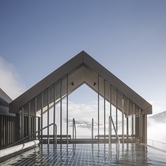 Hotel in Val Pusteria con spa per il vostro relax Piscina a sfioro con vista sulle montagne e copertura moderna sotto cielo limpido