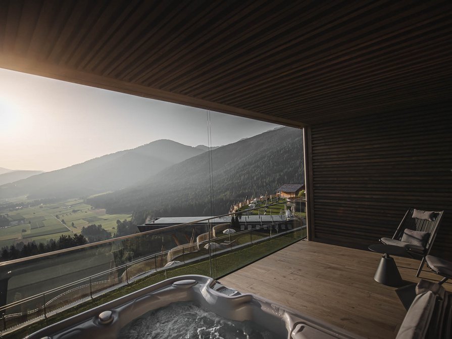 Il nostro hotel a Valdaora tra cielo e terra Balcone con vasca idromassaggio e sedie con vista sulle montagne al tramonto