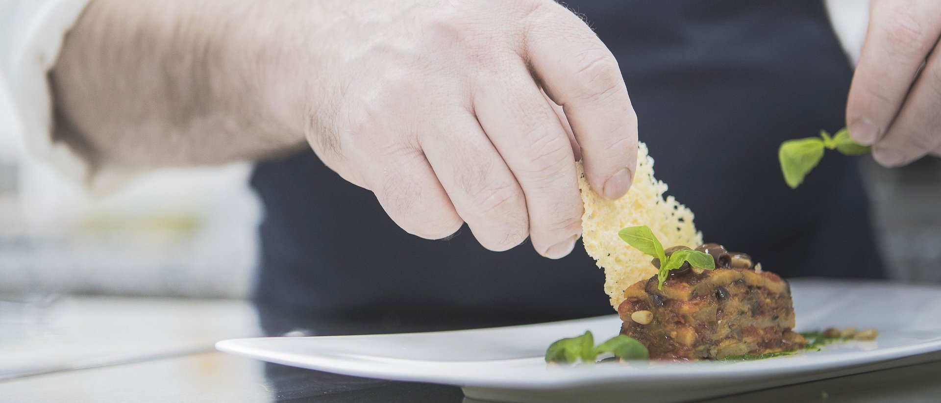 Hotel gourmet in Alto Adige per buongustai Cuoco decora piatto raffinato con croccante di formaggio ed erbe fresche