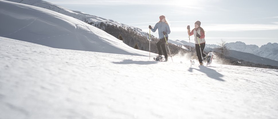 Ultime novità e storie da Valdaora Due persone fanno escursioni con racchette da neve in montagna innevata al sole