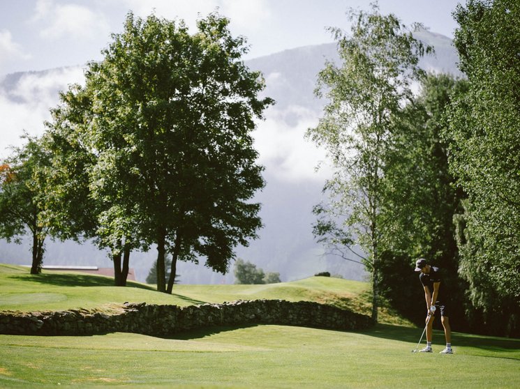 Golf Club Pustertal - Il tuo campo di golf a Plan de Corones Persona gioca a golf su un campo verde con alberi e montagne sullo sfondo