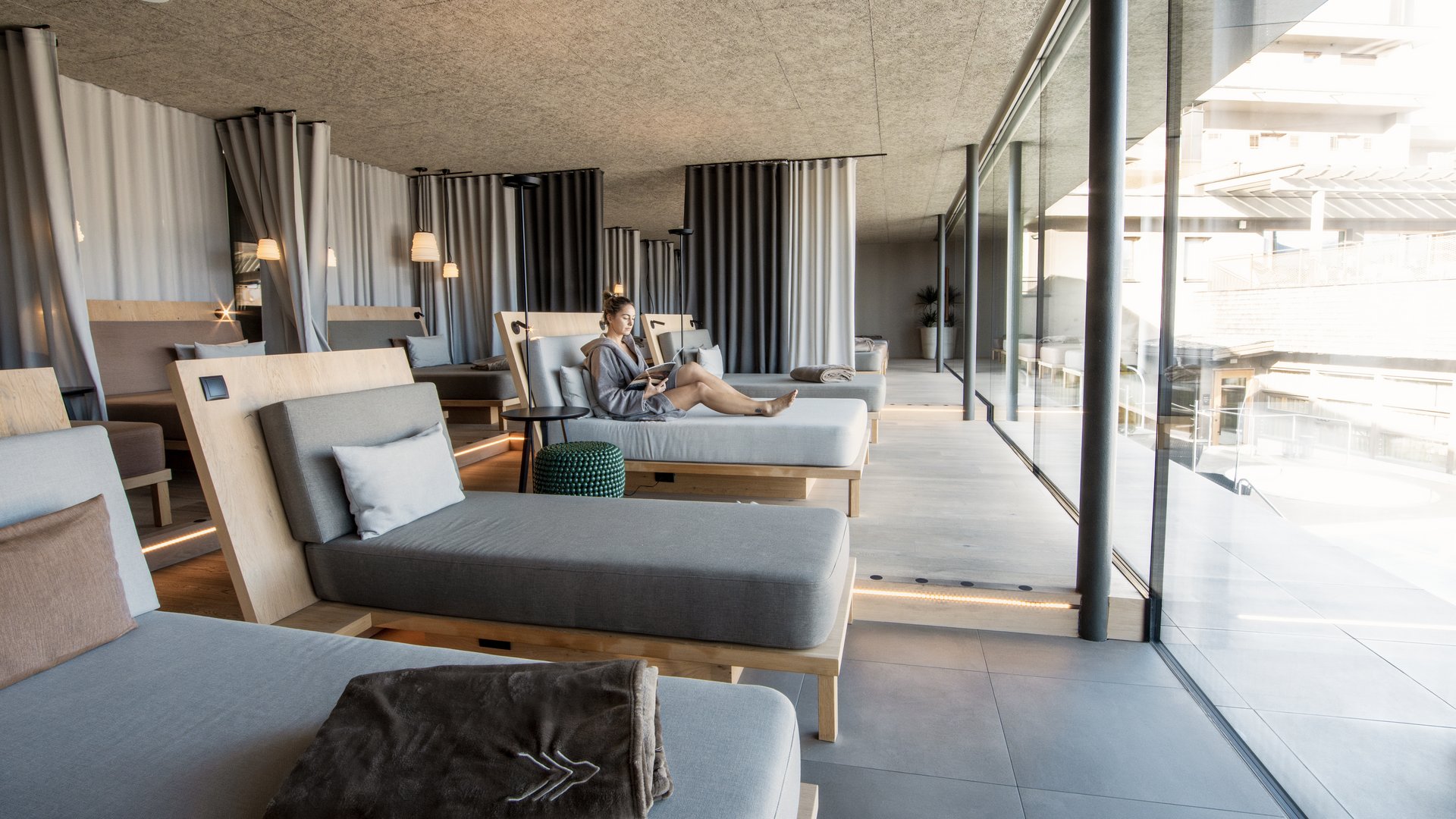 Le nostre saune in Val Pusteria vicino al Plan de Corones Donna rilassata su lettino in sala relax moderna con grandi finestre