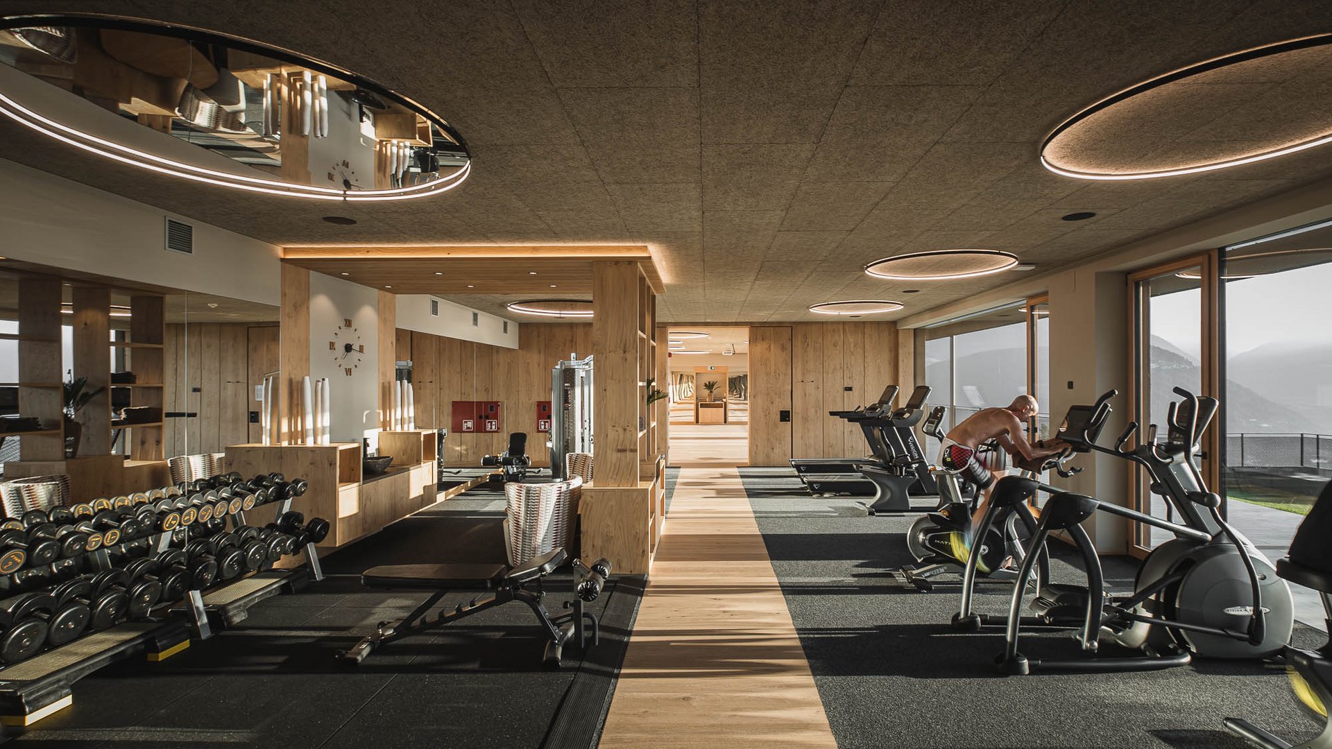 Il nostro hotel con palestra in Val Pusteria Sala fitness moderna con pesi e attrezzi cardio davanti a grandi finestre panoramiche