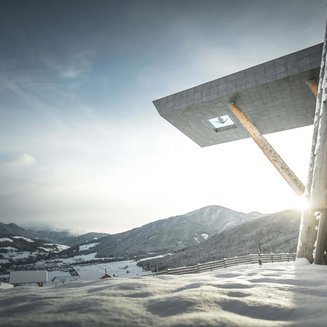 Shopping a Brunico e molto altro ancora Montagne innevate con edificio moderno e sole che sorge nella valle