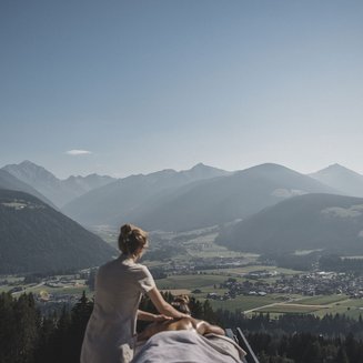 Das Wellnesshotel im Pustertal zum Entspannen Frau erhält Massage mit Blick auf Berge und Dorf