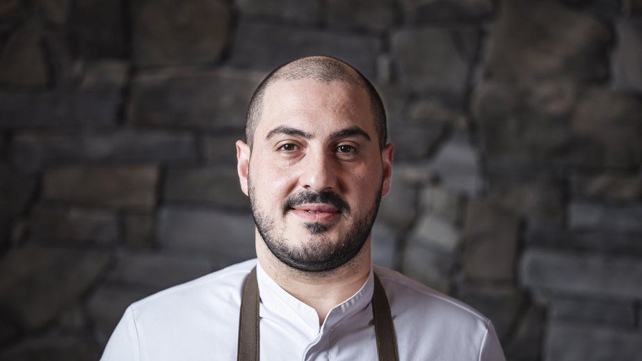 Unser Hotel in Olang zwischen Himmel und Erde Porträt eines Kochs in weißer Jacke und schwarzer Schürze vor Steinwand