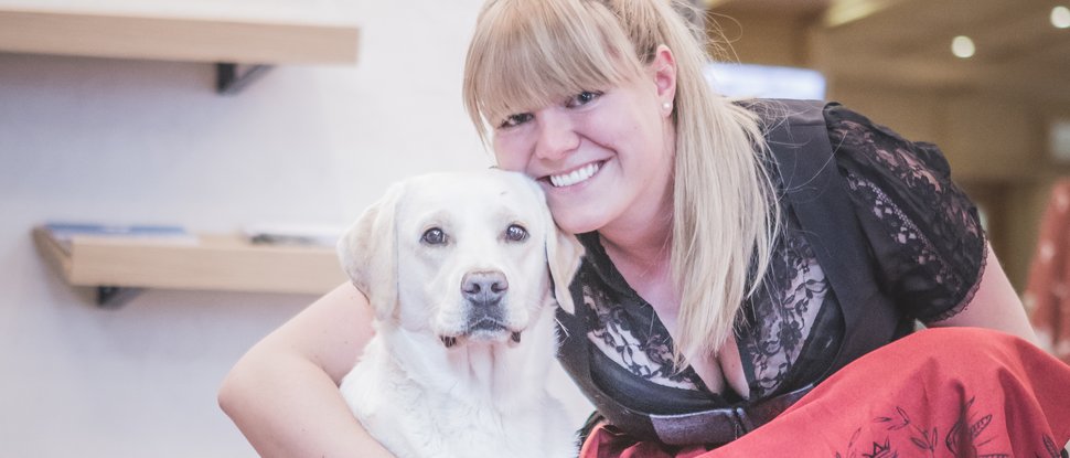 Aktuelle News und Geschichten aus Olang Eine Frau in traditioneller Kleidung umarmt einen weißen Labrador auf einem Teppich