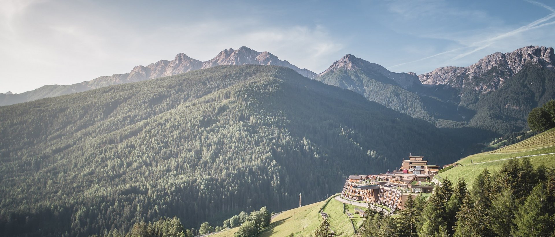 Hotel im Pustertal mit 5 Sternen Berglandschaft mit bewaldeten Hügeln und Ferienanlage am Hang
