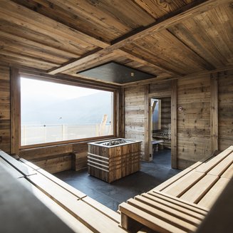 Das Wellnesshotel im Pustertal zum Entspannen Moderne Sauna mit Holzwänden, Bänken und großer Fensterfront mit Bergblick